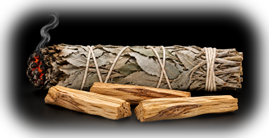 A smoldering white sage bundle beside three sticks of palo santo wood